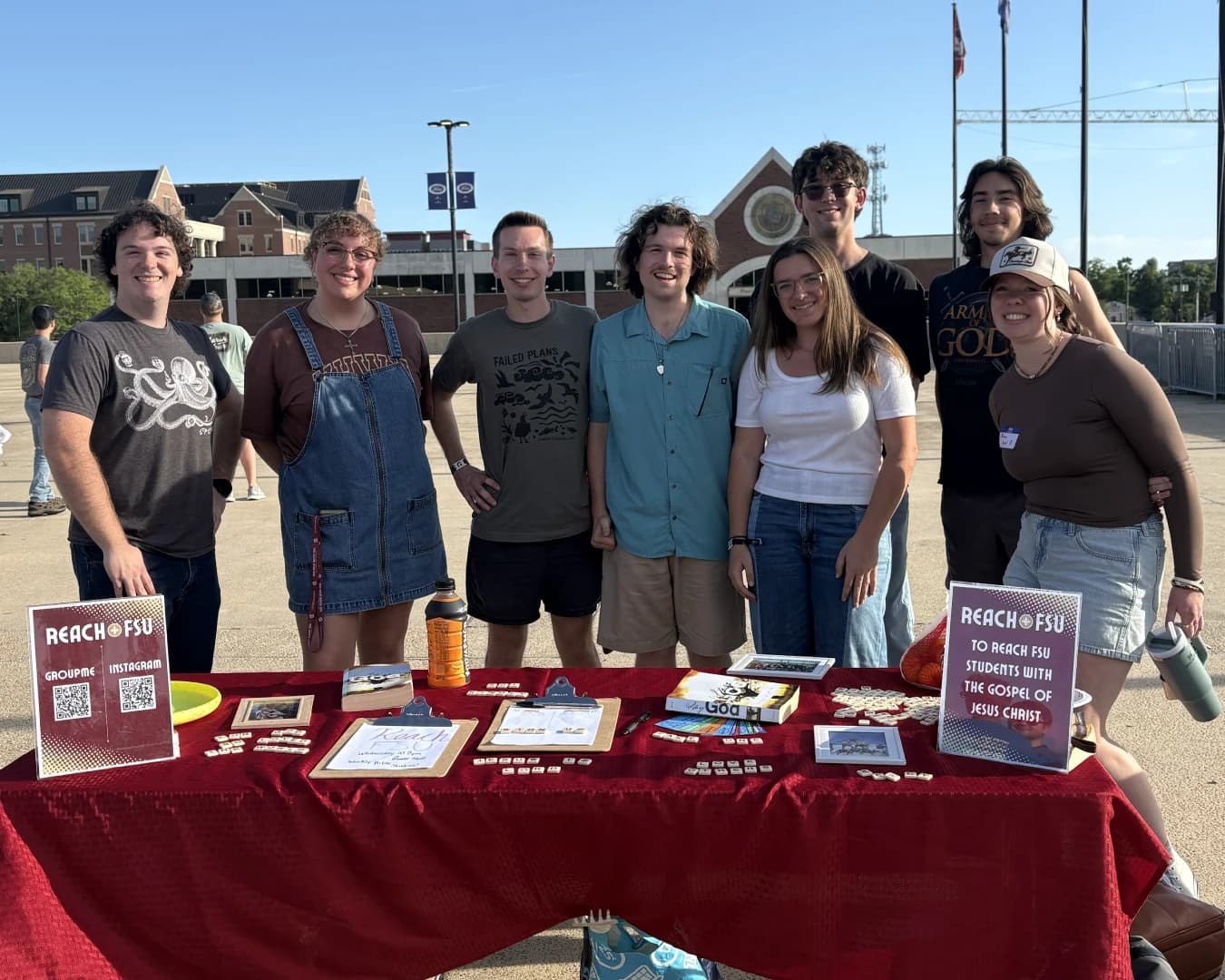 ReachFSU students standing behind their tabling setup on campus, a garnet-draped table of sign-up sheets and QR codes in front of them