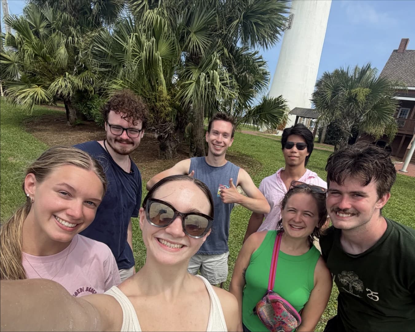 A group of ReachFSU students leaning into a selfie outdoors, palm trees behind them